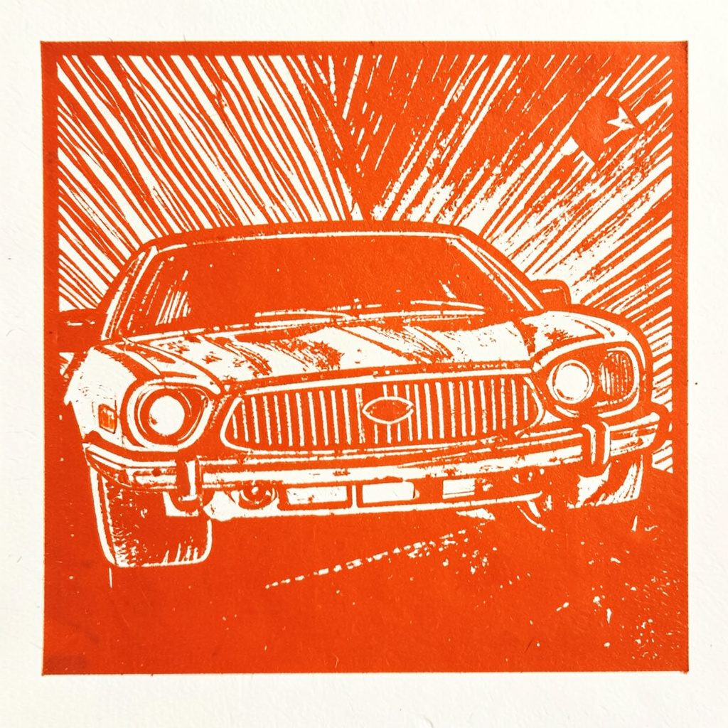 A carved linocut relief print of an open notebook and pen on a desk with rolling green grass and pale blue sky visible through a window behind it, rendered in earthy rust brown and olive tones with a calm studious mood